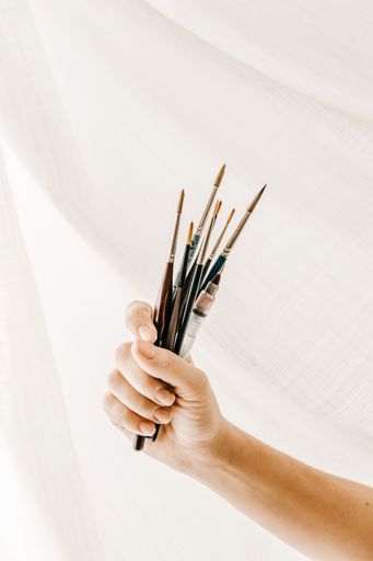 A vertical shot of a person holding a fistful of painting brushes