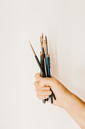 A vertical shot of a person holding a fistful of painting brushes
