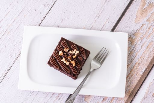 An overhead shot of a slice of chocolate cake topped with nuts on white ceramic plate with a fork