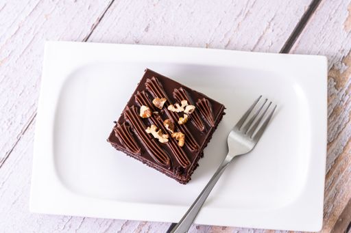 An overhead shot of a slice of chocolate cake topped with nuts on white ceramic plate with a fork