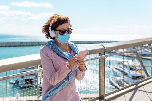 A middle-aged woman wearing a face mask standing on a bridge and listening to music
