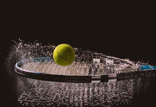 A closeup shot of a tennis ball and racket with a splash of water isolated on a dark background