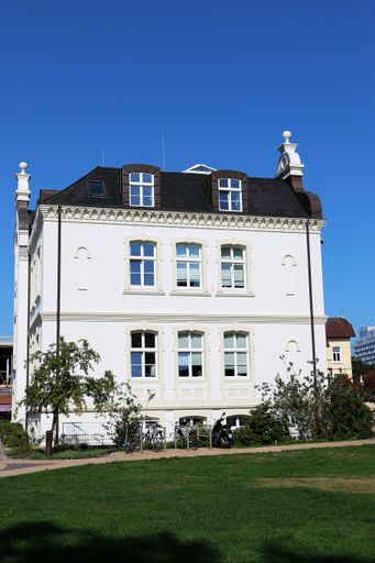 A vertical shot of a white mansion with a small park in front