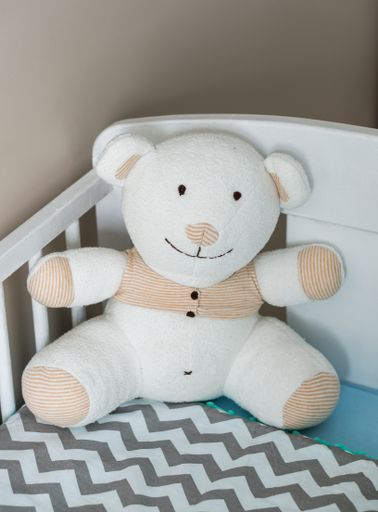 A closeup of a white, soft teddy bear in a baby crib