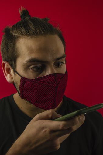 A vertical closeup shot of a surprised man looking at his phone while wearing a facemask - Coronavirus/Covid-19 theme