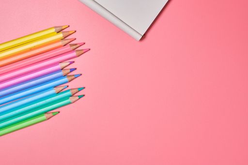 A top view of a notepad and colored pencils on a pink background with copy space
