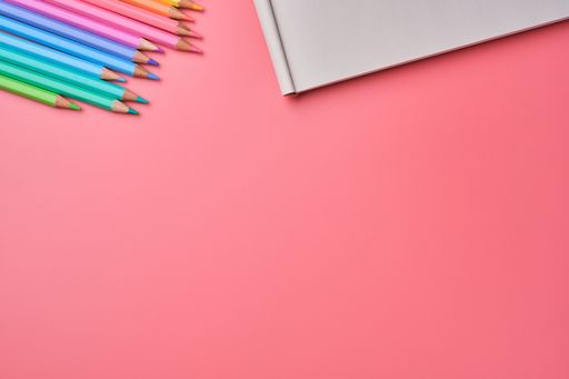A top view of a notepad and colored pencils on a pink background with copy space