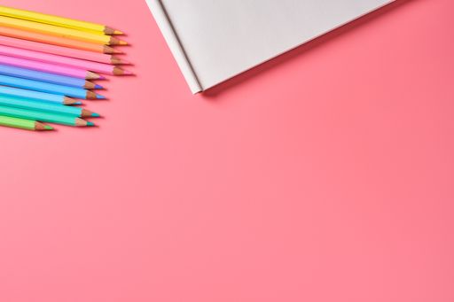 A top view of a notepad and colored pencils on a pink background with copy space