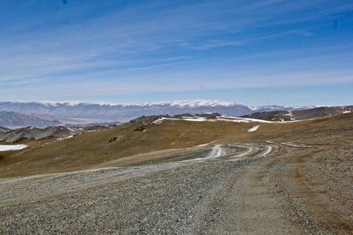 A dirt road through a mountainous landscape and blue sky in Mongolia