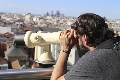 A selective focus shot of an attractive caucasian male admiring Madrid through a telescope