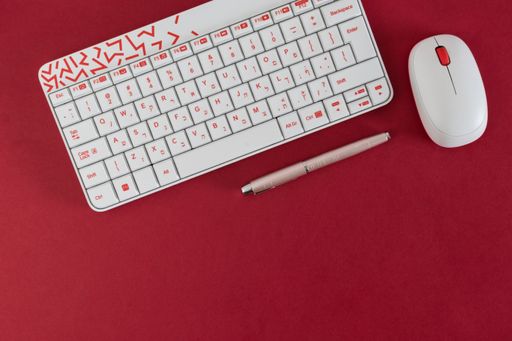 A top view of white keyboard. a pen and mouse on the red background