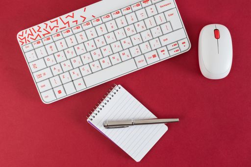 A closeup shot of a white keyboard and mouse with notebook and pen isolated on red background,