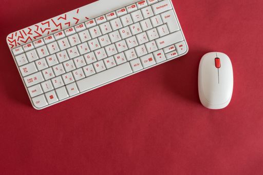A flat lay of a modern white keyboard with a wireless mouse on a red surface