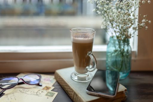 A selective focus shot of a tall glass cup with a cappuccino in front of a window