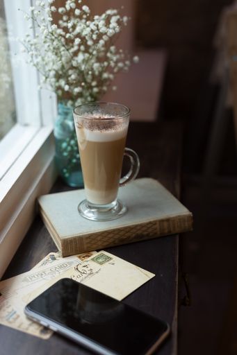 A selective focus shot of a tall glass cup with a cappuccino in front of a window