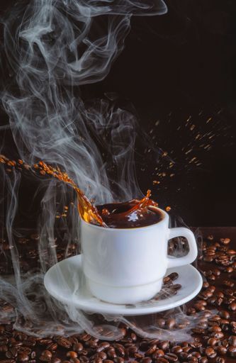A vertical shot of a mug with coffee drops being poured from it with beans on the table on a dark background