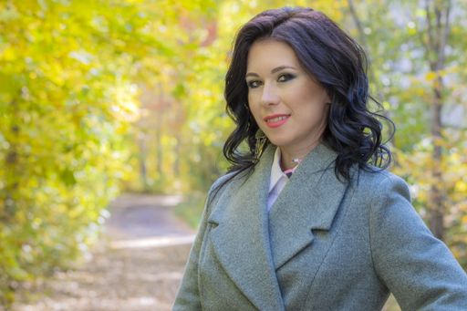 A closeup portrait of an attractive smiling brunette woman standing with a beautiful autumn scene behind