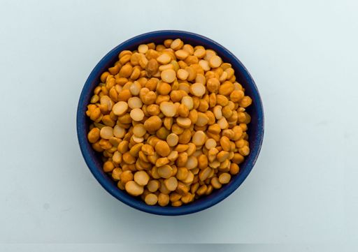 A bowl containing yellow split chickpeas on a white background