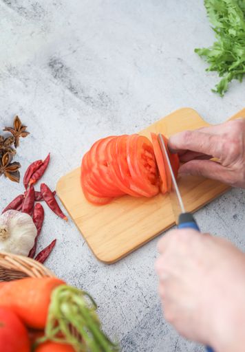 A Vertical shot of a chef slicing tomatoes on a wooden board