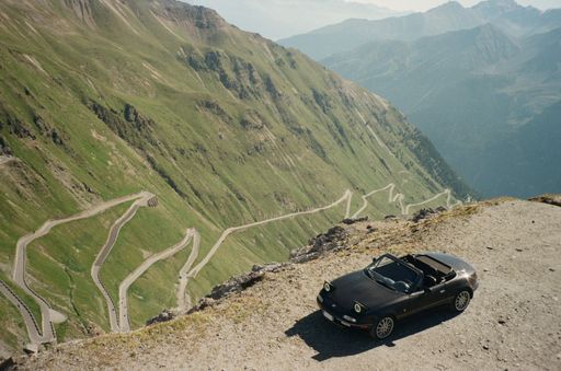 An aerial view of the black retro car on a high hill on a mountainous background