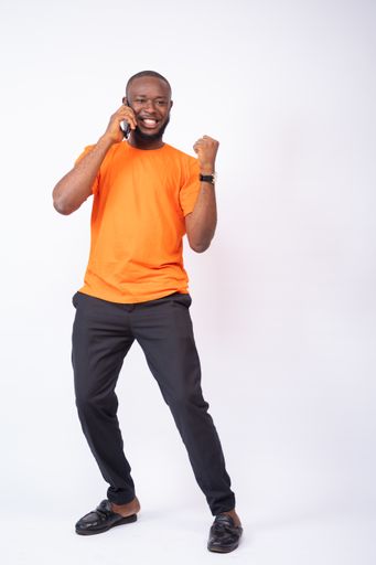 An excited young Nigerian man celebrates while making phone call isolated on a white background