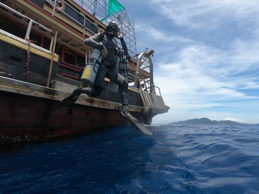 a scuba diver jumping into blue water from a boat