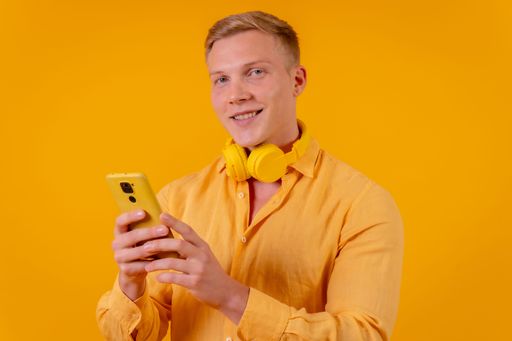 A Blond Caucasian man selecting music with phone in yellow background