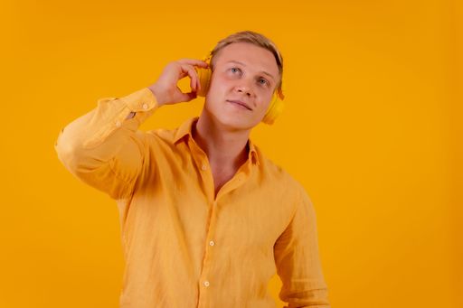 A blond Caucasian man with a cell phone and wireless headphones listening music in yellow background