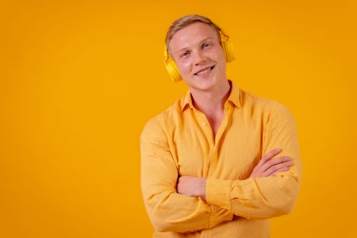 A blond Caucasian man with a cell phone and wireless headphones listening music in yellow background