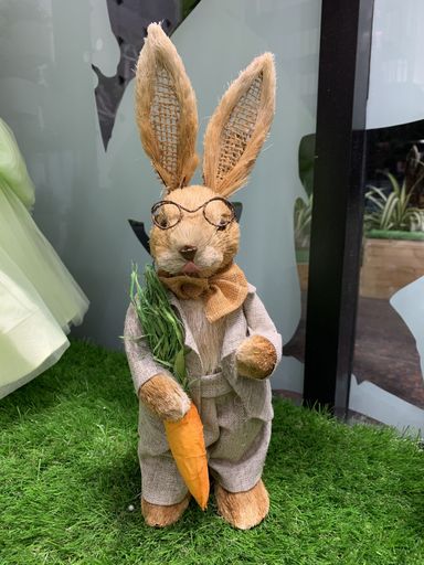 a vertical shot of a brown rabbit toy standing on a grassy floor holding a carrot