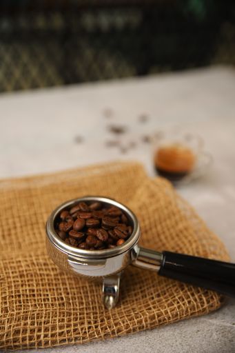 A vertical shot of a portafilter with roasted coffee beans on a sackcloth