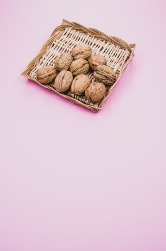 A vertical shot of walnuts on wicker basket isolated on a pink background