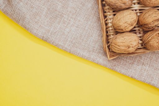 A top view of walnuts on wicker basket on a burlap pouch  isolated on a yellow background