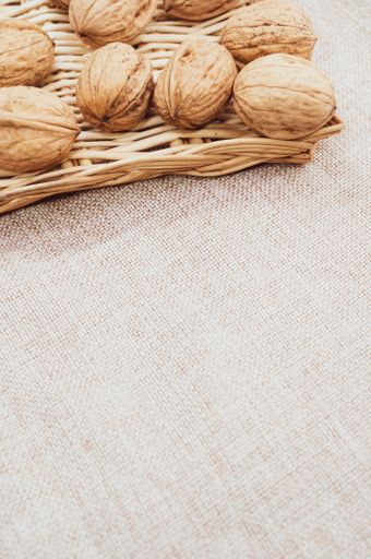 A vertical shot of walnuts on wicker basket on a burlap pouch