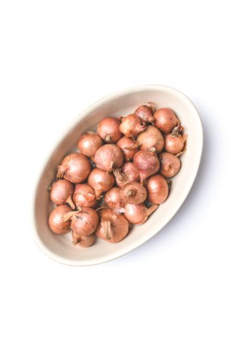 A vertical overhead shot of a bowl of raw shallots on a white surface