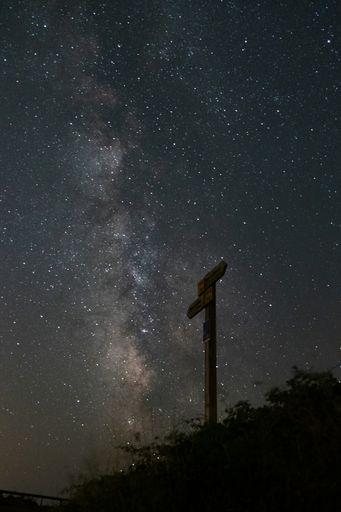 A vertical shot of a wooden sign pointing the milky way