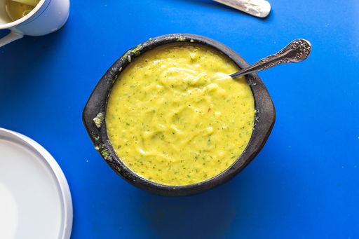 A high angle shot of guacamole in a bowl with a spoon on a blue surface