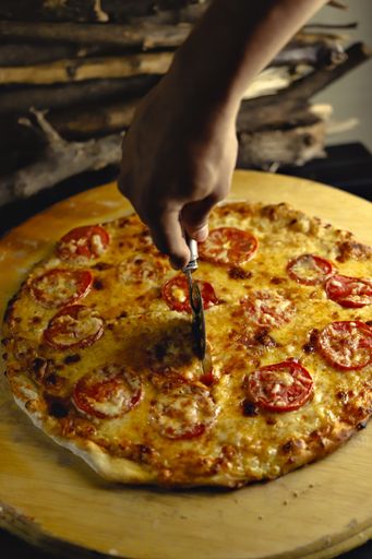 A vertical shot of a person cutting a delicious pizza with tomatoes and melted cheese
