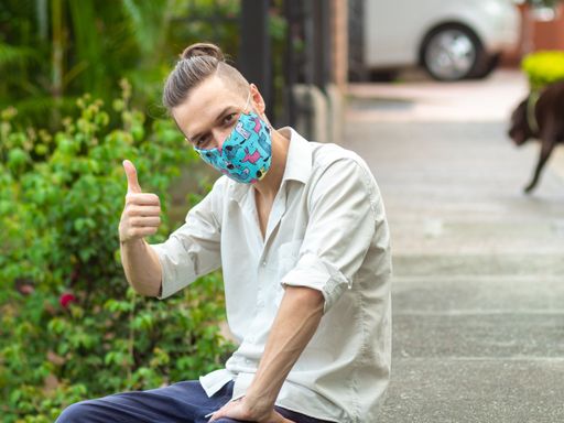 Caucasian Young Man Sits on the Sidewalk Using a Handcraft Face Mask Says Ok with his Thumb up