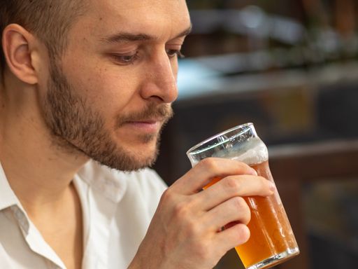 Caucasian Young Man in White Shirt Drinks Red Handcraft Beer in Large Glass