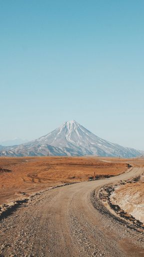A beautiful vertical shot of a narrow curvy and muddy road with an amazing high mountain in the background