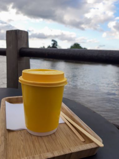 A vertical shot of a plastic cup on a tray by a lake