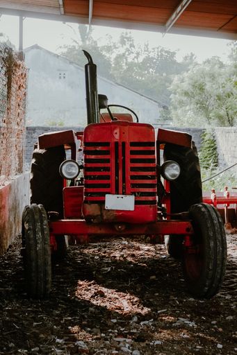 A vintage red old antique tractor in an old shed with farm tools