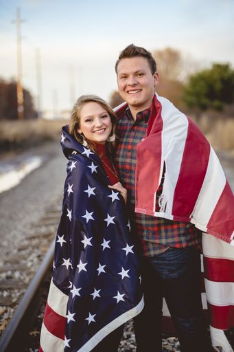 A vertical shot of a couple hugging with the united states flag around them and smiling at the camera