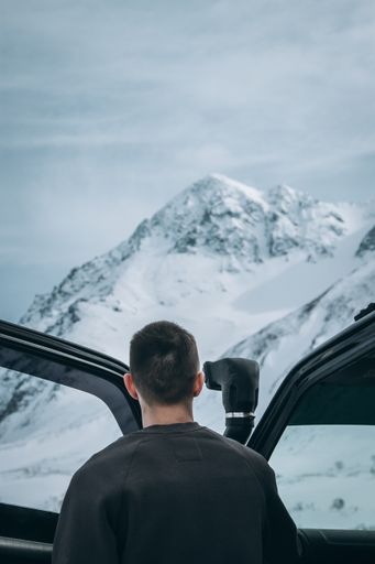 A male standing beside his 4x4 car and looking at beautiful snowy mountains in the Alps
