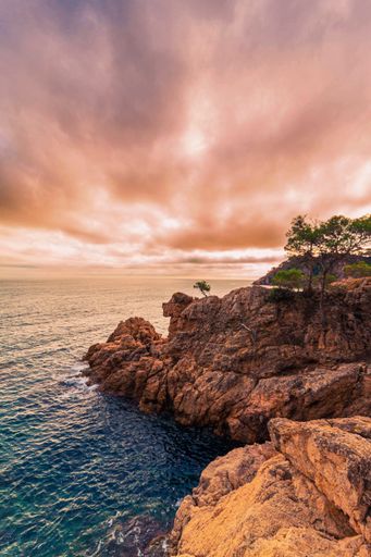 A vertical drone shot of sunset over the rocky coast of a sea