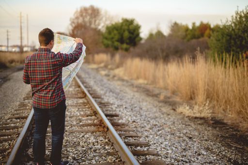 A shallow focus shot of a male standing on train tracks while looking at the map