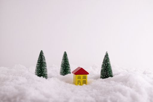 A closeup of a house and fir-trees, funny toy figurines in the snow