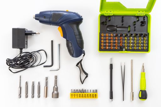 A top view of a cordless electric screwdriver with various construction tools on the white surface