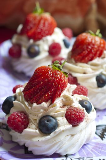 A vertical closeup of creamy cupcakes with strawberry, raspberry and blueberry garnish